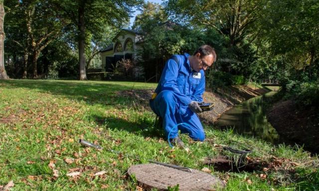 Medewerker van IMD meet bij een rioolput in een park in Apeldoorn